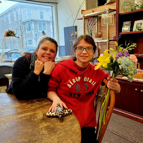 Woman in black and woman in red Aeropostal sweatshirt, holding flowers and smiling