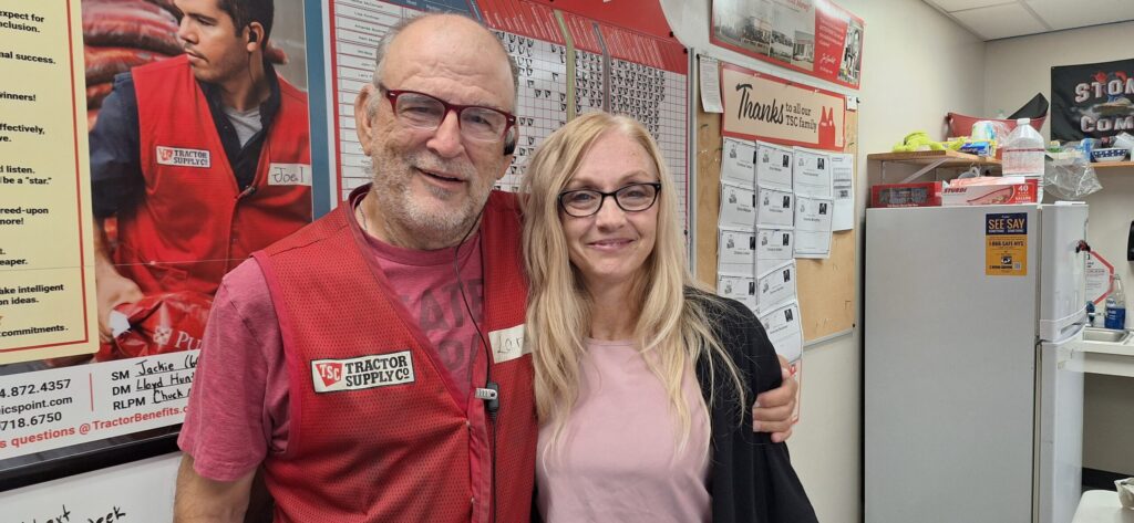 Man in glasses and red work vest with his arm around blond woman.